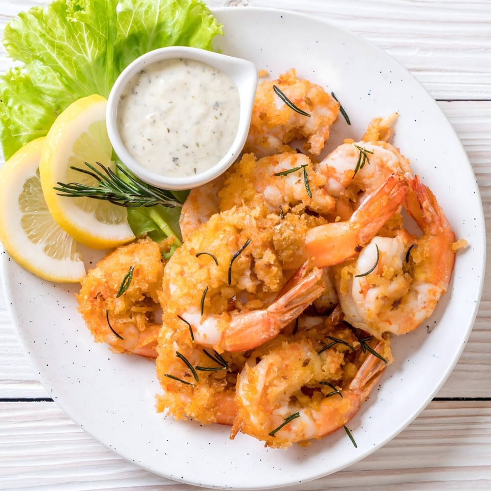 Crispy fried shrimp with lemon slices, lettuce, and a side of creamy dipping sauce.