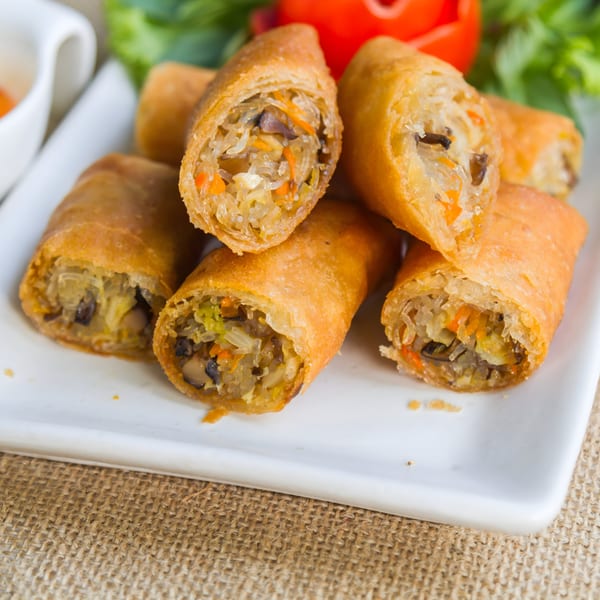 Crispy Asian spring rolls, some cut open to show the vegetable and noodle filling, on a white plate.