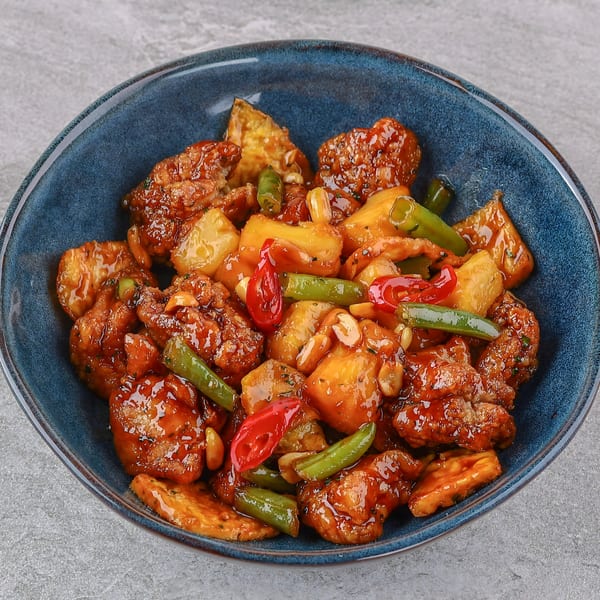 Sweet and sour chicken with pineapple, green beans, red peppers, and peanuts in a blue bowl.