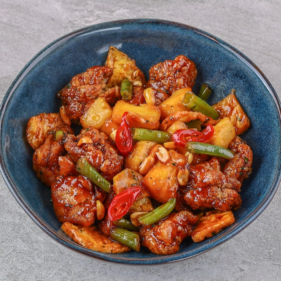 Sweet and sour chicken with pineapple, green beans, red peppers, and peanuts in a blue bowl.