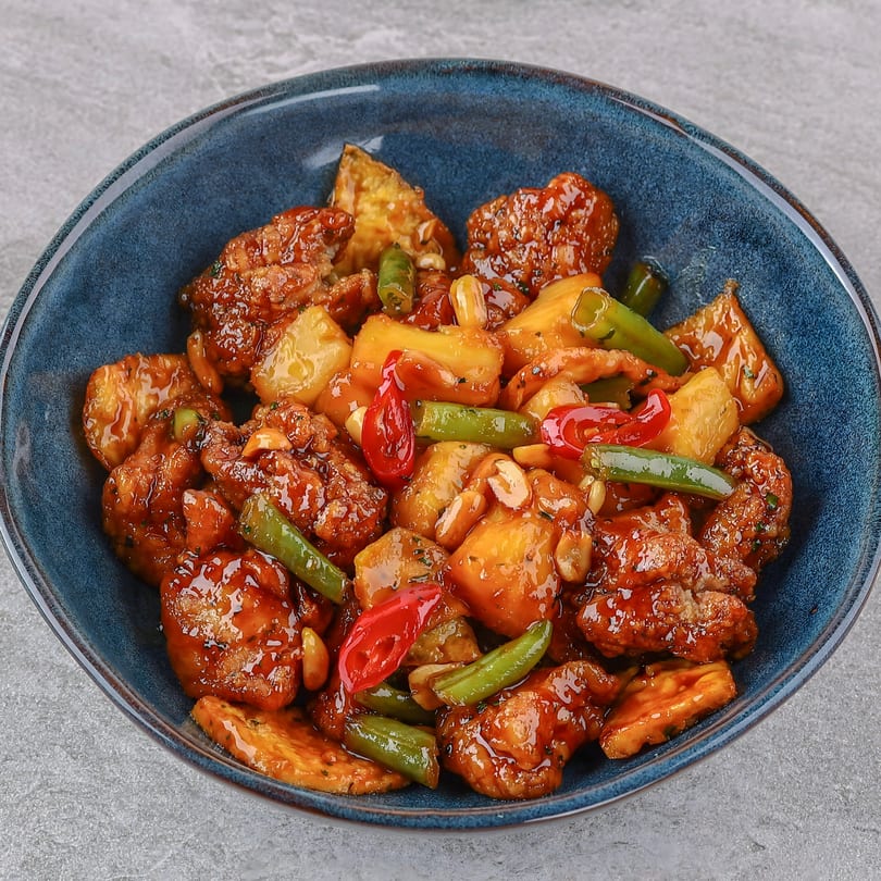 Sweet and sour chicken with pineapple, green beans, red peppers, and peanuts in a blue bowl.