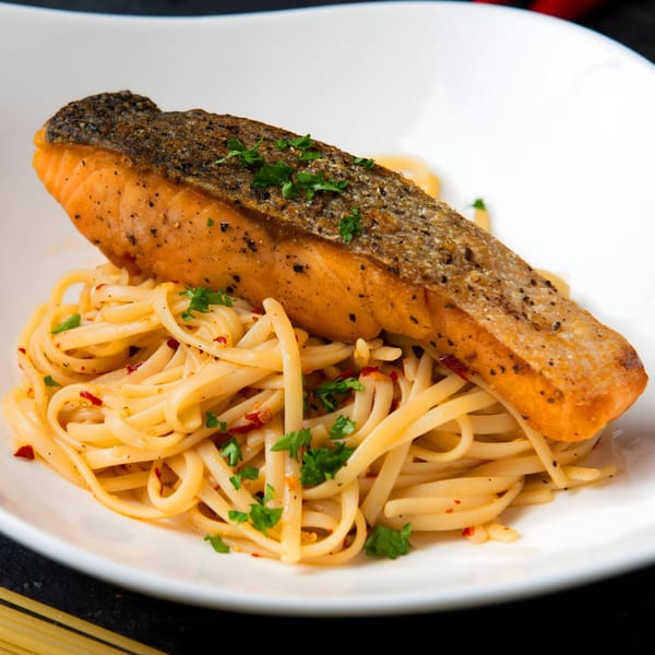 Crispy-skinned salmon fillet resting on a bed of linguine pasta with herbs and chili flakes.